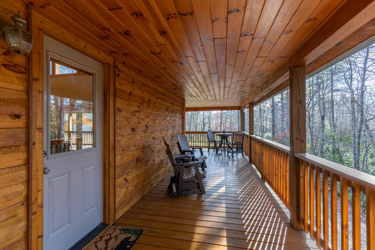 An inviting transition area with wooden rocking chairs and a dining table, opening directly toward the outside. The open door and view through the windows blend the indoors with the tranquil outdoor scenery, establishing a sense of flow between cozy interior comfort and the natural surroundings.