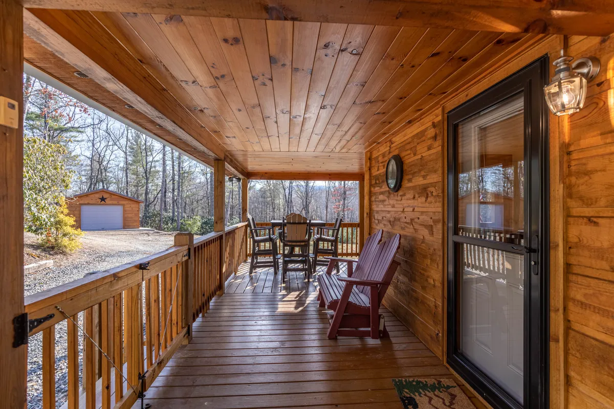 A cozy wooden porch lined with Adirondack chairs and a dining table, surrounded by trees. The porch is bathed in sunlight, suggesting a perfect spot for relaxing after a day of outdoor exploration.