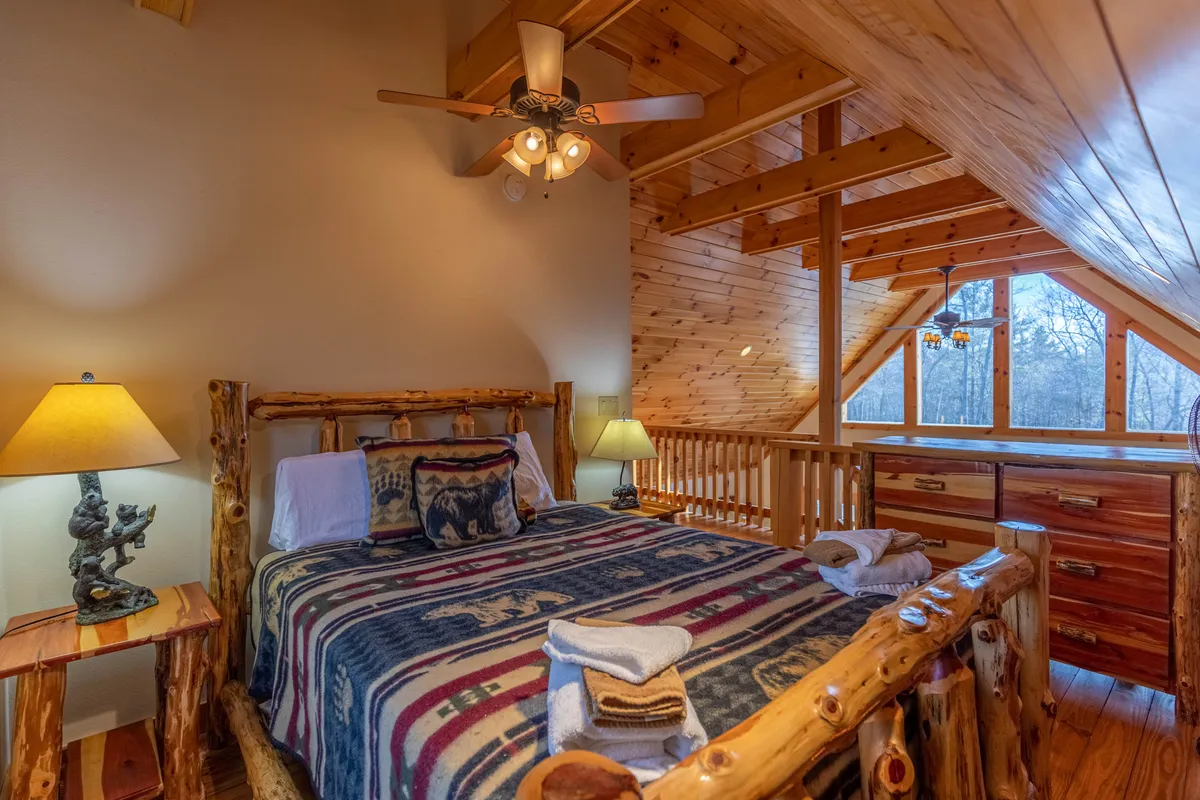 A cozy bedroom with a log bed, decorative throw, wooden furnishings, and expansive windows looking out onto the natural surroundings. The setup provides a restful spot to unwind after a day of outdoor exploration.
