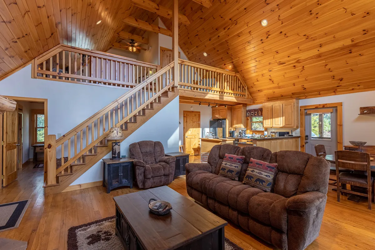 An open-plan living space with a wooden staircase, comfortable seating area, kitchen, and dining table. Natural light streams in, suggesting a seamless flow between activities like cooking, dining, and relaxing together.