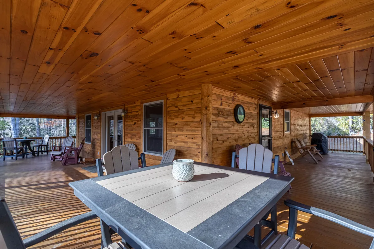 A covered outdoor dining area featuring a wooden ceiling, a sturdy dining table, and comfortable chairs, all set amidst a natural mountain backdrop. Decorative touches like a vase add to the inviting atmosphere, ideal for both intimate meals and enjoying the outdoors.