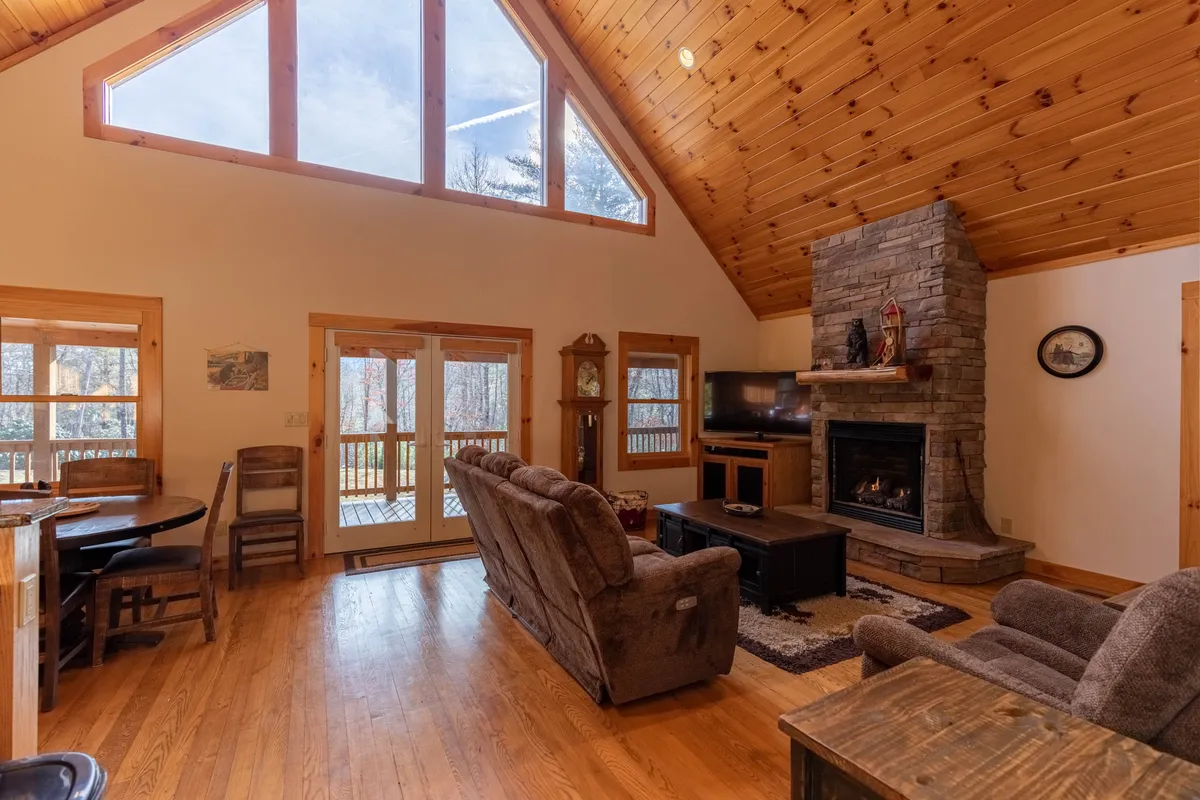A spacious lodge interior featuring a fireplace, large windows allowing for views of the outdoors, a wooden ceiling, and a central dining table. The scene exudes a welcoming, communal vibe—ideal for sharing meals, playing games, or relaxing together after a day of adventure.